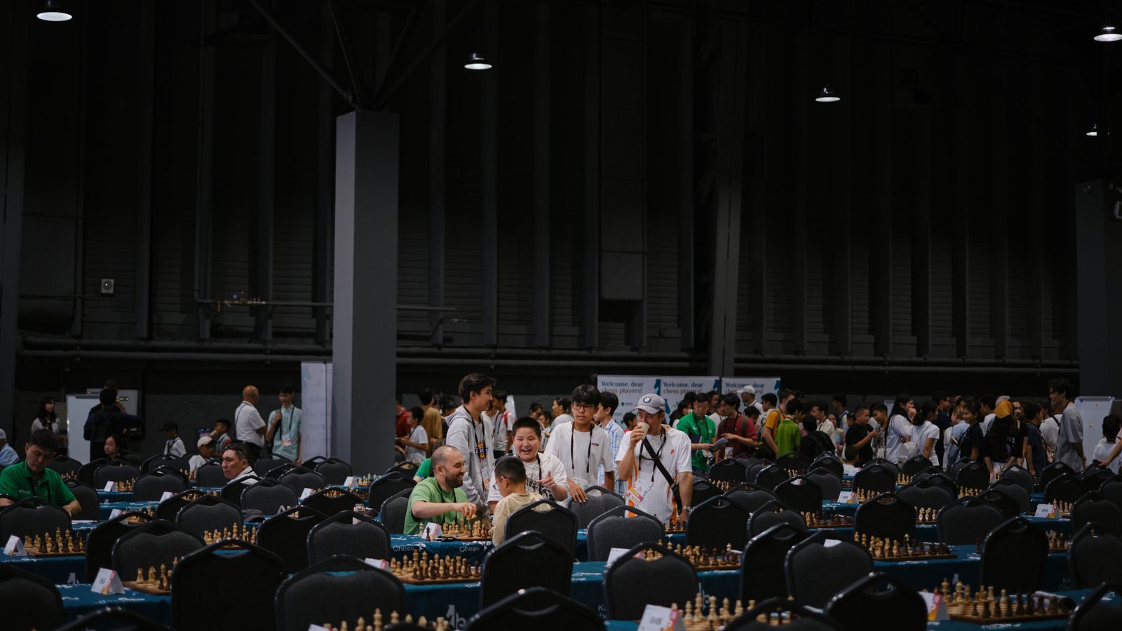 A tournament hall filled with chess boards and players between rounds.