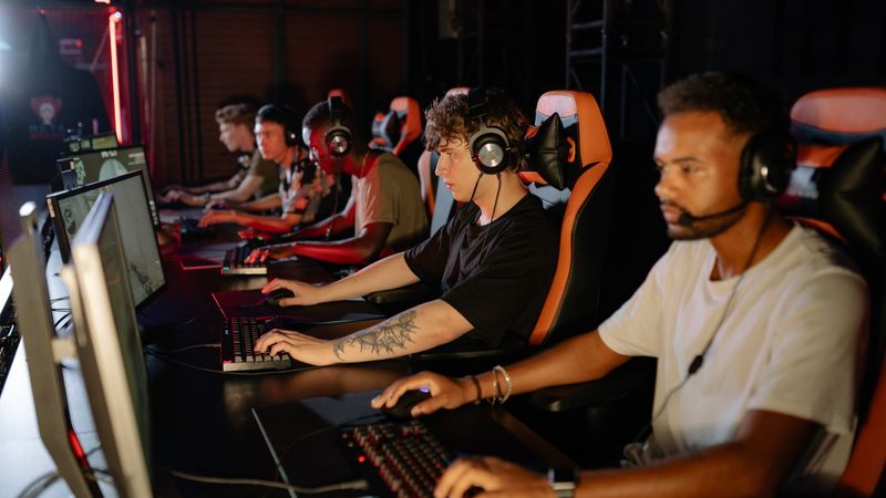 A row of players at computers in a tournament room, headsets on, mid-match.